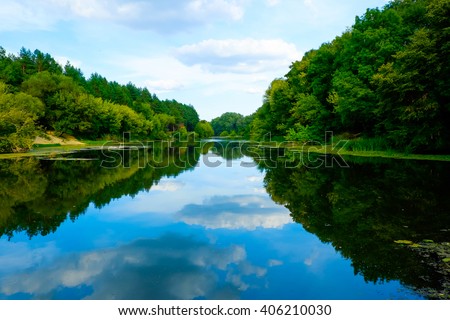 Beautiful wild nature park, forest. River or lake with mirror reflections and clear water on sunny day. Amazing wilderness nature landscape panorama. Quiet river in surroundings greenery in summer.