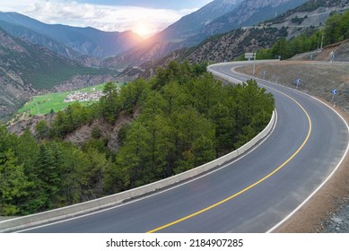 Beautiful winding mountain asphalt road with a perfect S curve, highway in the mountains with sunrise beams and rural village in Tibet, China