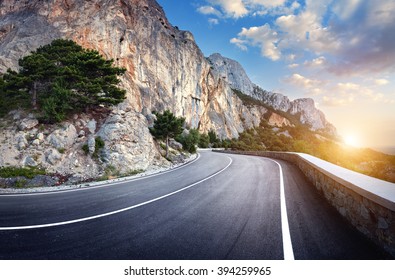Beautiful winding mountain road with a perfect asphalt with high rocks and colorful sunset in summer. 