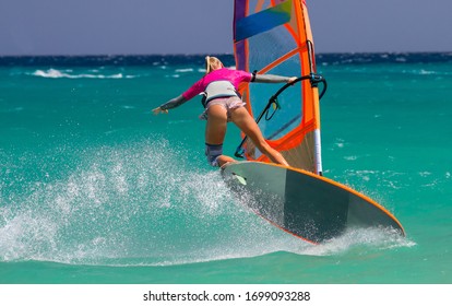 Beautiful windsurfer girl in bikini with board and sail windsurfing at strong windy day over turquoise water. Atlantic Ocean, Canary Islands, Fuerteventura,  Sotavento