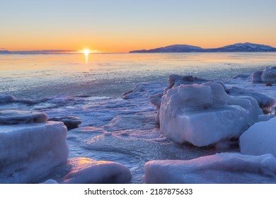 Beautiful winter arctic seascape. The sun sets over the horizon. Ice-covered seashore and unfrozen water. Large ice floes on the shore. Sunset landscape with sea coast. Cold weather. Northern nature.