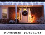 Beautiful winter blizzard night. House main entrance and porch decorated with glowing lights for winter holidays. Night scene with fresh snow. Christmas and New Year holiday background.