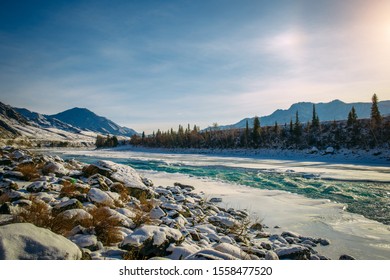 Beautiful winter landscape, mountain river valley in fantastic sunlight. Turquoise river runs among snow-covered banks with coniferous forest. Unfrozen area on the ice-bound mountain river.