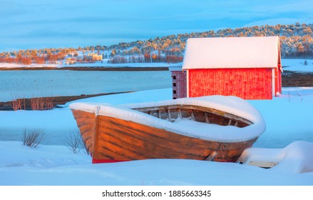 Beautiful Winter Landscape With Old Fishing Red Cabin (boathouse) Boat At Sunset - Red Wooden Boathouse And Boat Covered With Layers Of Snow - Tromso, Norway