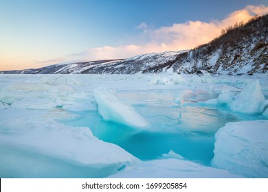 Beautiful winter landscape with sea, ice, and coast. Large cracks and water among ice floes and hummocks. Traveling and Hiking in nature.  Sea of ​​Okhotsk, Magadan Region, Siberia, Far East Russia. - Powered by Shutterstock