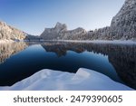 Beautiful winter landscape view of a snow-capped mountain range reflecting in a lake with a snow dune in the foreground