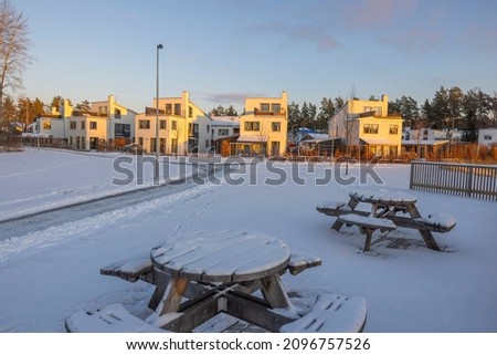Beautiful winter  landscape view of walkway leading to suburban houses across of resting place with wooden tables and benches on a  at sunset. Sweden.