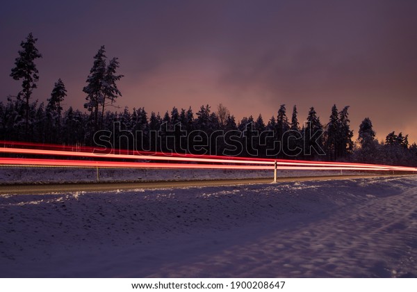 Beautiful winter night driving motion on a\
road by forest trees with car light\
trails