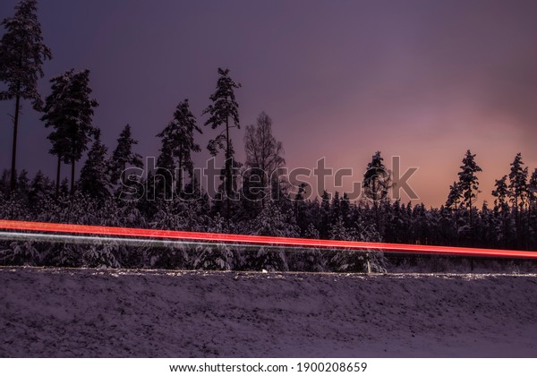 Beautiful winter night driving motion on a\
road by forest trees with car light\
trails
