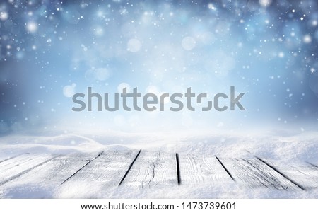 Beautiful winter snowy blurred defocused blue background and empty wooden flooring. Flakes of snow fall and sparkle on light, copy space.