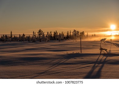 Beautiful Winter View From The Top Of A Swedish Mountain With Low Growing Trees, A Snow Mobile Trail Passing Into The Orange Setting Sun