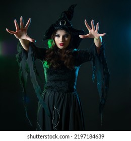 beautiful witch with hat make spell. Halloween party, witches ' Sabbath. Young beautiful brunette in witch costume, greenish backlight, dark background - Shutterstock ID 2197184639