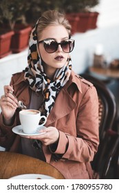 Beautiful Woman 24-25 Year Old Drinking Coffee In Cafe Wearing Stylish Jacket, Sun Glasses And Silk Scarf Outdoors. Autumn Season. 