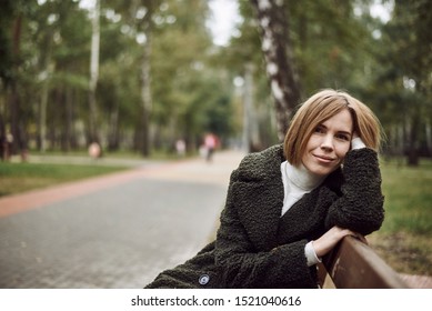 Beautiful Woman 35-45 Years Old Sits On A Bench In The Park In Autumn.