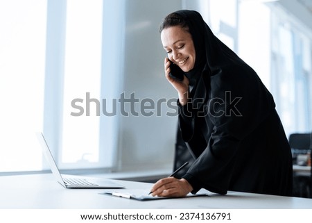 beautiful woman with abaya dress working on her computer. Middle aged female employee at work in a business office in Dubai. Concept about middle eastern cultures and lifestyle