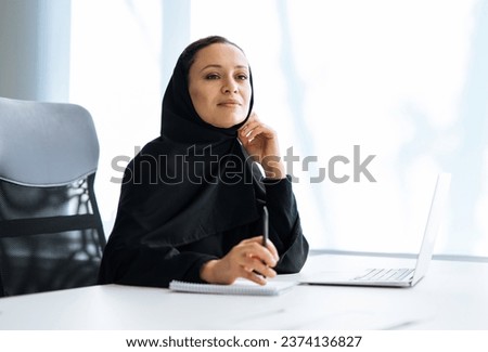 Beautiful woman with abaya dress working on her computer. Middle aged female employee at work in a business office in Dubai. Concept about middle eastern cultures and lifestyle