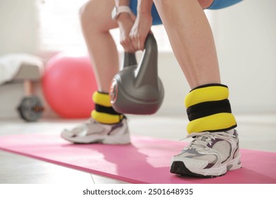 Beautiful woman with ankle weights and kettlebell training indoors