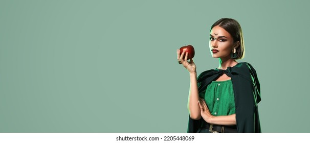 Beautiful woman with apple dressed as witch for Halloween on green background with space for text