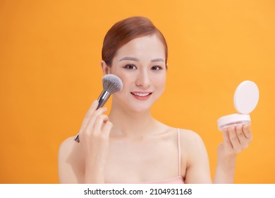 Beautiful Woman Applying Blusher To Her Cheek With A Large Cosmetics Brush While Holding A Compact Mirror In Front Of Her