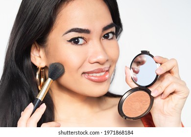 A beautiful woman applying a bronzer make up.