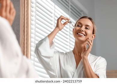 Beautiful woman applying cosmetic serum onto her face near mirror in bathroom - Powered by Shutterstock