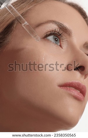 Beautiful woman applying cosmetic serum onto her face, closeup