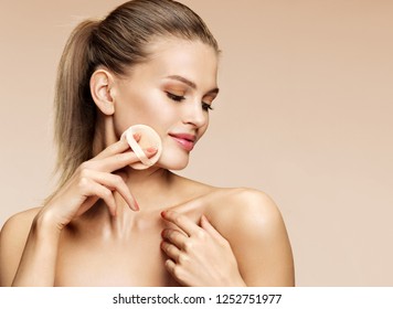 Beautiful woman applying dry powder using cosmetic cushion on her facial skin. Photo of attractive girl with perfect makeup on beige background. Beauty concept