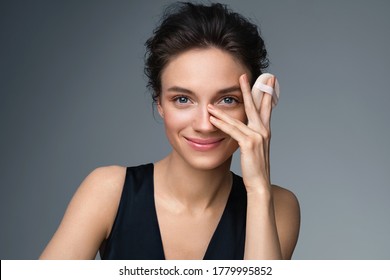 Beautiful woman applying dry powder, using cosmetic cushion on her facial skin. Photo of woman with perfect makeup on gray background. Beauty concept