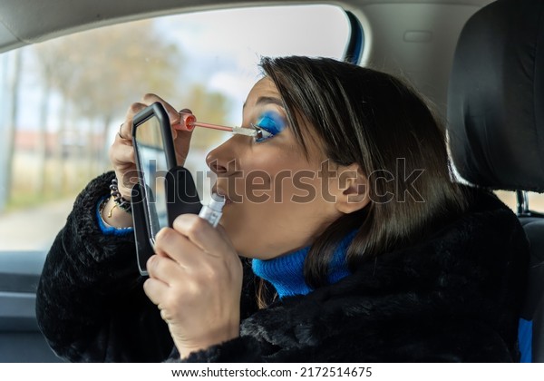 beautiful woman applying eye make-up in the car\
with a mirror