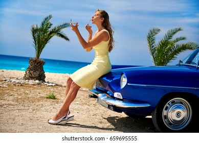 Beautiful woman applying lipstick near retro cabriolet car on the tropical beach. Idyllic scenery - Powered by Shutterstock