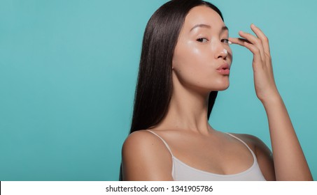 Beautiful woman applying moisturizer to her nose against blue background.. Woman applying beauty cream on her face.