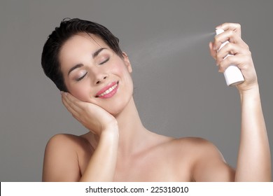 Beautiful Woman Applying Spray Water On Face On Neutral Background