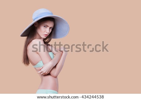 Beautiful woman in a bathing suit and hat on BEIGE BACKGROUND. slender young woman in a bathing suit, studio picture   