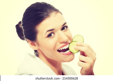 Beautiful Woman In Bathrobe Holding Slices Of Cucumber Trying To Eat Them. Isolated On White.