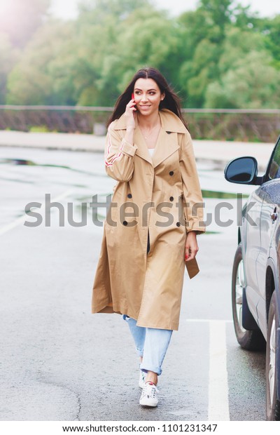 Beautiful woman in the beige coat talks\
by the phone on the street, soft focus\
background