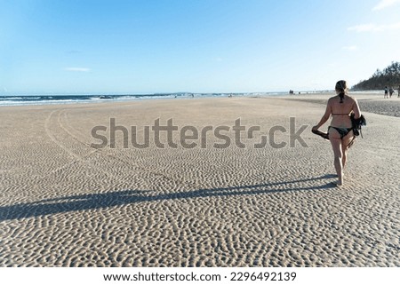 Beautiful woman in a bikini and hat, from the back, walking on the beach sand. Guaibim Beach, Valenca, Bahia.