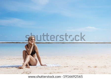 Beautiful woman in bikini on tropical beach. Female tourist sunbathing on summer vacation, smiling and feeling happy on carribean paradise island with beautiful turquoise ocean landscape behind.