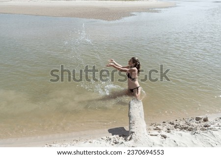 Beautiful woman in a bikini in a river throwing water into the air. Person on vacation and travel. Taquari Beach in Valenca, Brazil.