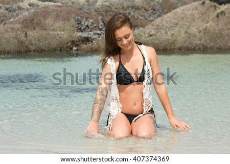 Beautiful woman in bikini sitting in the ocean with hands in the water
