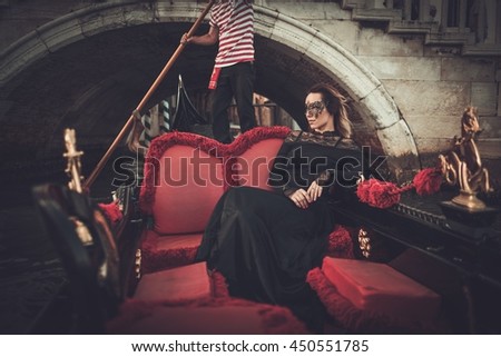 Beautiful woman in black dress with carnaval mask riding on gondola. 