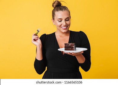 Beautiful Woman In Black Dress Happily Holding Plate With Slice Of Chocolate Cake In Hands Over Yellow Background. Plus Size Model