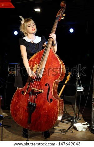Beautiful woman in black dress plays wooden contrabass in night club.
