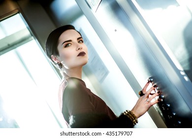 Beautiful Woman With Black Hair And Dark Lipstick Standing In The Elevator And Waits For The Floor Pressing A Button