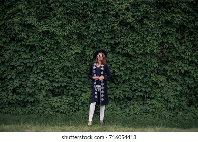 Beautiful Woman In Black Jacket Against Greenery Garden Wall 