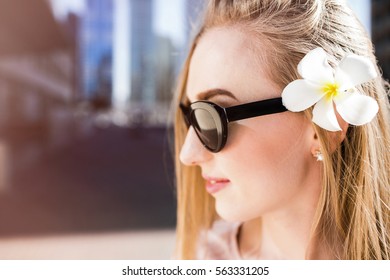 Beautiful woman in black sunglasses from Prada poses  with white flower in her hair