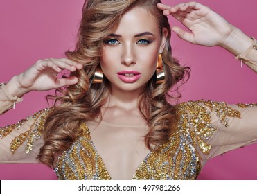 Beautiful woman blonde fashion model in gold dress with perfect make up. Isolated on a pink background.
