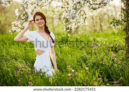 Beautiful woman in a blooming spring garden in a light dress smiling looking at the camera