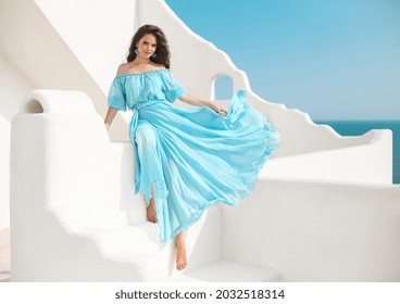 Schöne Frau in blauem Kleid auf dem Dach der Insel Santorini, Griechenland. Fashion Outdoor Foto von schönen Mädchen Modell im Sommer Urlaub, genießen mit Blick auf das Meer.