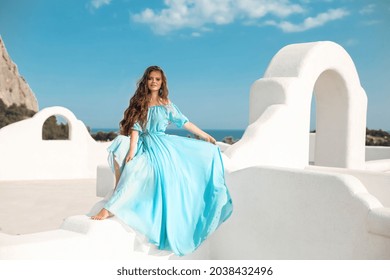 Schöne Frau in blauem Kleid auf dem Dach der Insel Santorini, Griechenland. Fashion Outdoor Foto von schönen Mädchen Modell im Sommer Urlaub, genießen mit Blick auf das Meer.