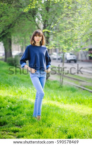 beautiful woman in blue enjoys the spring sun on a background of young leaves in the city